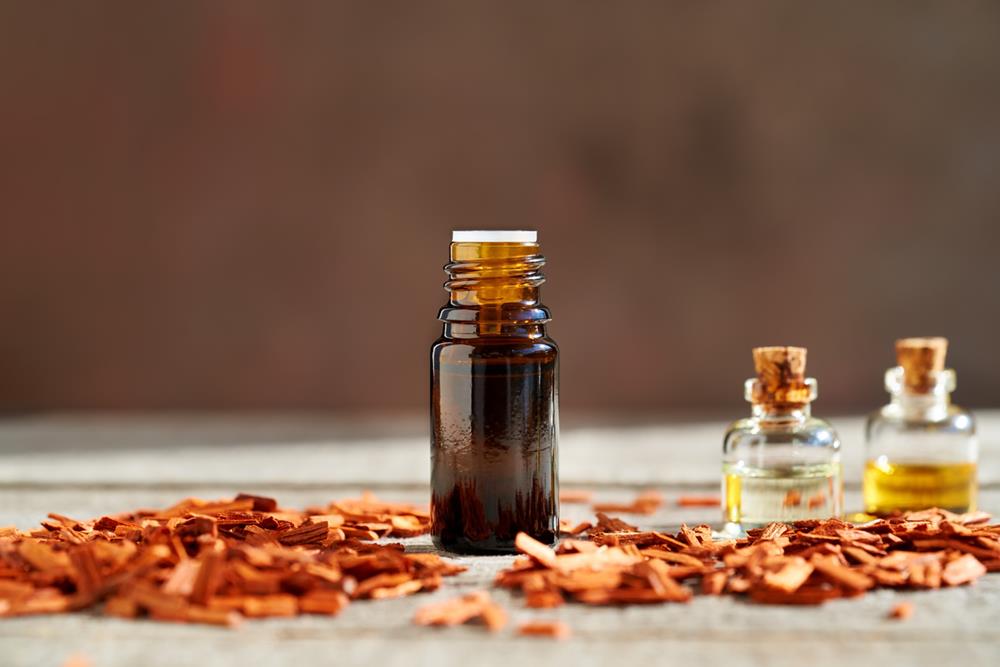 A bottle of sandalwood essential oil with red sandalwood chips on a table