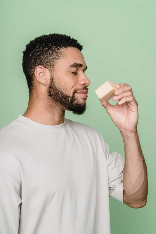 a man in a crew neck shirt holding a soap bar and smelling it