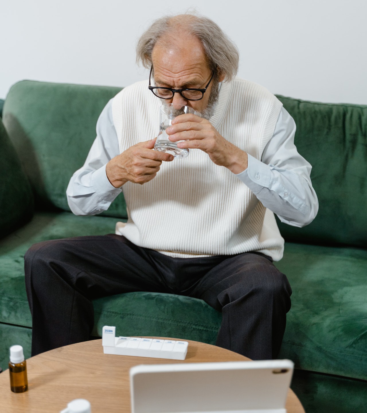 elderly man taking his medicine while sitting on green couch