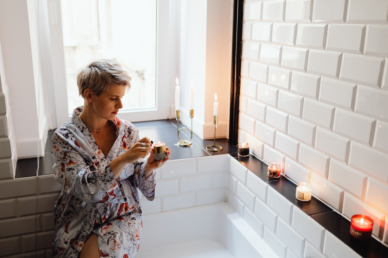man lightning a scented candle wearing a printed bathrobe sitting on bathtub