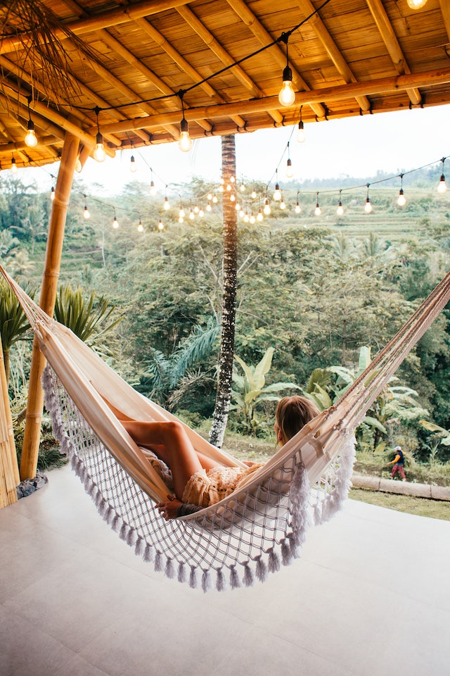 slender woman resting in hammock under glowing garlands